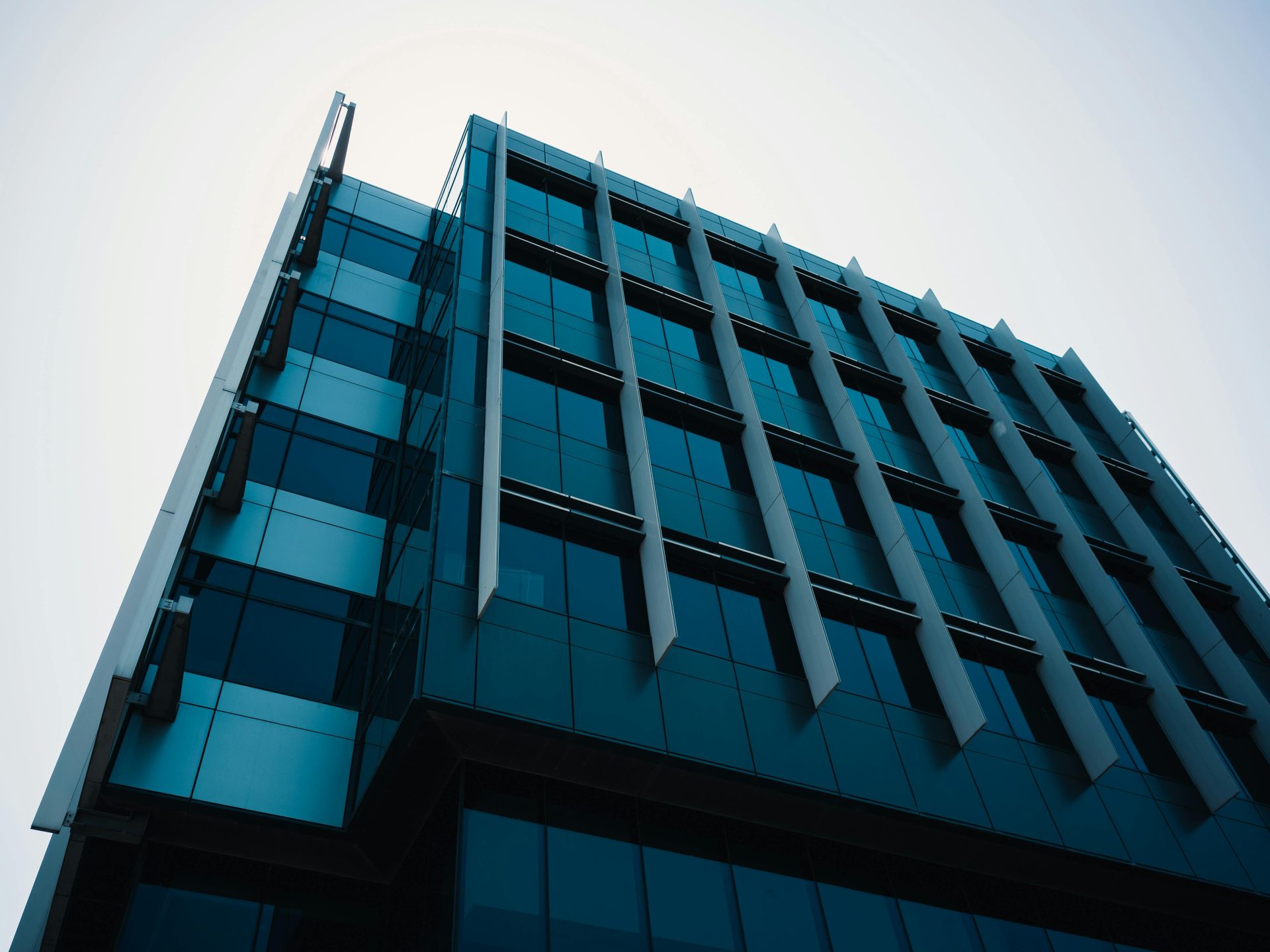 Ansicht von unten auf ein modernes Bürogebäude mit Glasfassade und geometrischer Gestaltung in urbaner Umgebung.