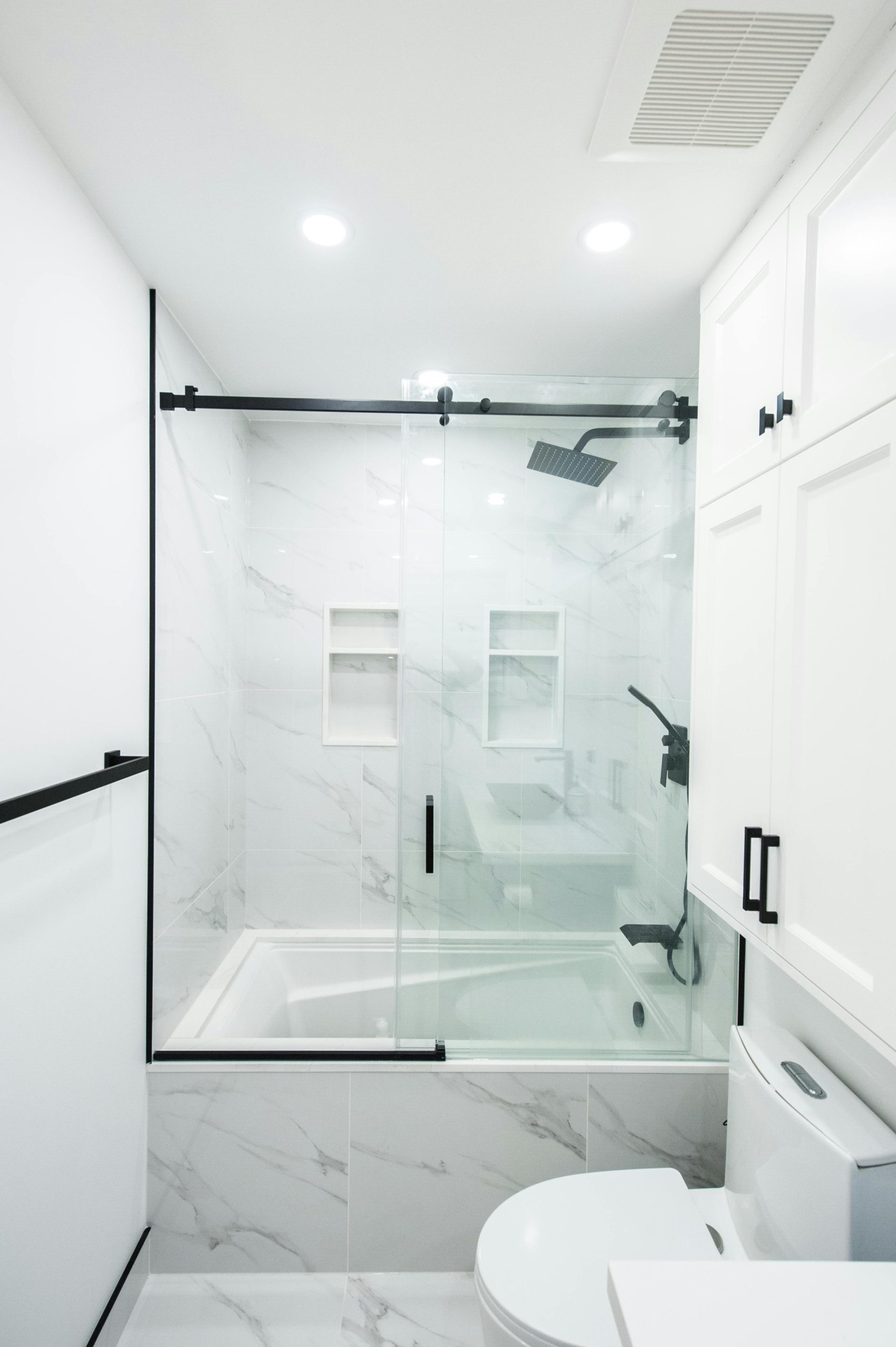 Elegantes und modernes Badezimmer mit weißen Marmorfliesen, Glasduschtüren und schwarzen Akzenten.